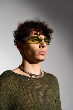 Kıvırcık saçlı, son moda güneş gözlüklü, kendine güvenen genç bir adam stüdyoda şık bir kıyafet giyiyor..