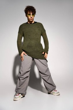 Şık kıvırcık saçlı genç bir adam stüdyoda güneş gözlüğü ve şık bir kıyafet takıyor..