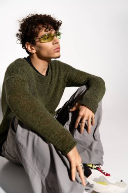 Şık kıvırcık saçlı bir adam, modaya uygun bir kıyafetle, modern modaya uygun bir şekilde poz verir..