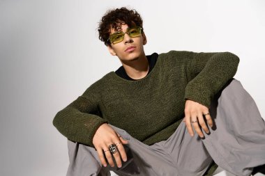 Kıvırcık saçlı ve güneş gözlüklü modaya uygun genç bir adam stüdyoda dinleniyor..