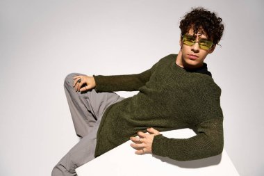 Kıvırcık saçlı ve güneş gözlüklü şık genç bir adam benzersiz tarzını stüdyoda sergiliyor..