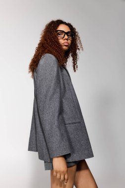 Genç ve güzel bir kadın, kendine güvenen cesur gri ceketiyle eşsiz tarzını sergiliyor..