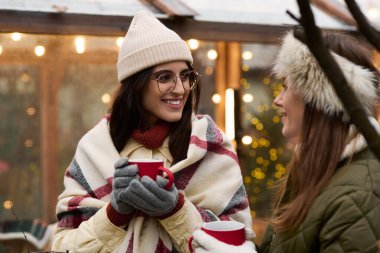 İki kadın kışın dışarıda sıcak içeceklerin tadını çıkarırken sıcacık kıyafetler içinde kahkahalar ve sıcaklığı paylaşıyor..