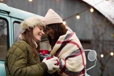 Battaniyeye sarılı iki kadın sıcak içkileri paylaşırken sevgiyle gülümsüyor, aşkı kutluyorlar..