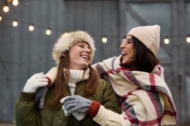 İki kadın, kış kutlamalarında sıcacık kıyafetlerini giyerken neşe dolu kahkahalarını paylaşıyor..