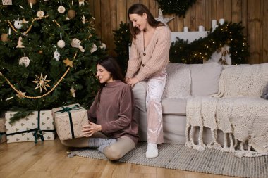 Konforlu kıyafetler içindeki iki kadın, güzel dekore edilmiş bir ağacın yanında keyifli bir tatil anlarını paylaşıyorlar..