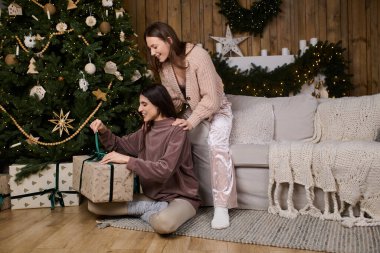 İki kadın kapalı alanda hediyelerini verirken ve gülüşürken rahat bir tatil atmosferinin tadını çıkarıyor..