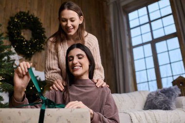 Samimi giyinmiş iki güzel kadın kışı birlikte kutluyor, bir hediye açtıklarında neşeyle..