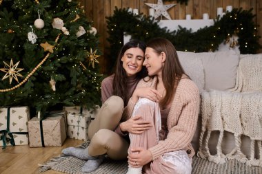 Güzel dekore edilmiş bir tatil ağacının yanında rahat elbiseli iki kadın eğleniyor..