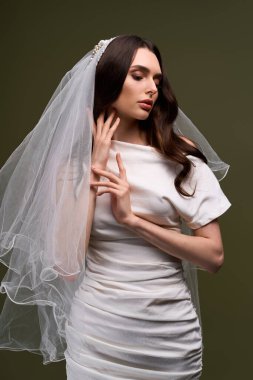 Genç bir gelin baş döndürücü bir gelinlik içinde parıldıyor, narin bir duvakla tamamlanmış..