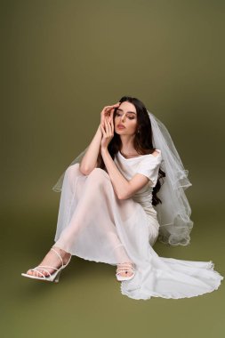 Süzülen peçeli genç gelin zarif bir şekilde oturur, huzurlu bir ortamda neşe ve zarafet saçar.