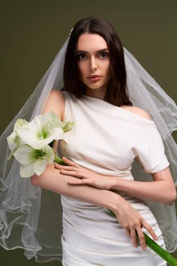 Genç bir gelin zarif bir şekilde poz verir, güzelliğini vurgular ve güzel bir çiçek tutar..