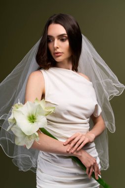 Genç bir gelin mutluluk ve zarafet saçar. Yumuşak ışıkla çerçevelenmiş çarpıcı bir çiçek tutar..