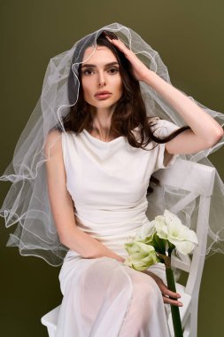 Güzel elbiseli genç bir gelin çiçekleri kucağında, zarifçe oturuyor ve neşeyle parlıyor..