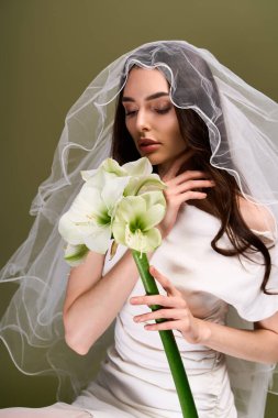 Güzel gelin zarafet sergiliyor, narin çiçekleri tutarken huzurlu düşüncelerde kayboluyor..