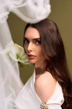 Büyüleyici genç gelin narin bir çiçekle güzelliğini sergiliyor, saf bir sevinç hissediyor..