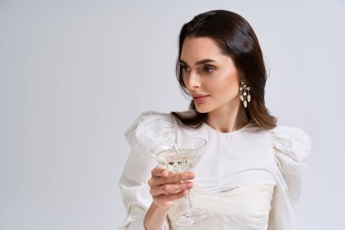 Genç gelin elinde bir şampanya kadehi tutuyor. Huzurlu bir atmosferde zarafet ve neşe saçıyor..