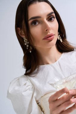 Göz kamaştırıcı, beyaz elbiseli bir gelin elinde bir bardak tutuyor ve düğün etkinliğinde mutluluğunu gösteriyor..