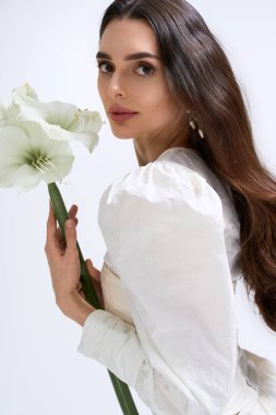 Gelin, neşe ve zarafeti somutlaştıran büyük beyaz bir çiçeği nazikçe tutarken ışıldıyor..