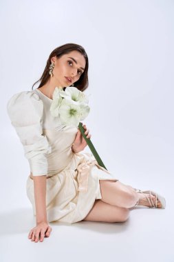 Güzel gelin, parlak bir stüdyoda zarifçe poz verirken çarpıcı bir çiçek tutuyor..