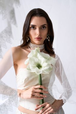 Genç gelin zarif bir mekanda çarpıcı beyaz bir çiçek tutarken güzelliğini sergiliyor..