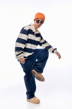 Modayı takip eden bir genç çizgili uzun kollu polo ve turuncu bir şapka giyer..