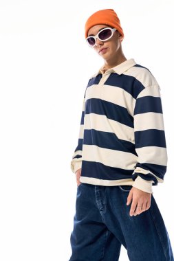 Şık bir genç, çizgili uzun kollu polo ve turuncu bir şapka giyerek kendine güvenerek poz verir..