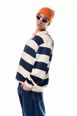 Bir genç, çizgili uzun kollu polo ve turuncu şapkayla güvenle poz verir..