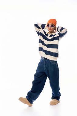 Modayı takip eden bir genç, çizgili uzun kollu polo ve turuncu şapka giyerek kendine güvenerek poz verir..