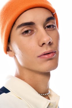 Genç, modaya uygun çizgili polo ve turuncu şapkalı beyaz arka planda rahatça poz veriyor..