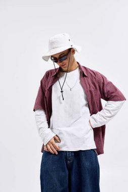 Modayı takip eden bir genç, kareli gömlek, güneş gözlüğü ve panama şapkasıyla rahatça poz verir..