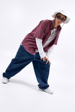 Moda meraklısı bir genç, temiz beyaz bir arkaplanda kendine güvenen bir şekilde poz verir..