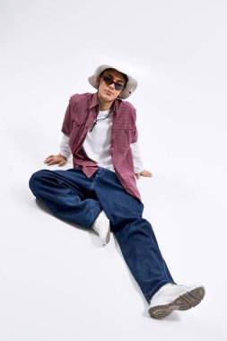 Ergen, uzun kollu ve şık bir panama şapkasının üzerine kareli bir gömlek giyer..
