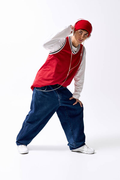 A trendy teenager in a red hat and baggy jeans strikes a dynamic pose against a white backdrop.