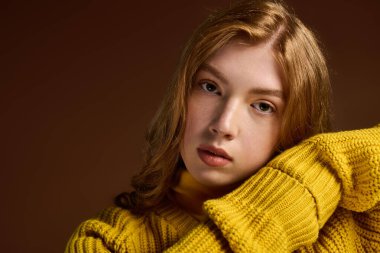 Kızıl saçlı genç bir kadın, rahat bir stüdyo ortamında şık bir kış süveteri mankenliği yapıyor..