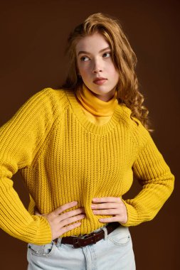 Kızıl saçlı bir kadın, kahverengi bir arka planda rahat bir kazakla kış modasını sergiliyor..