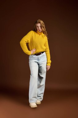 Kızıl saçlı bir kadın, sıcacık bir kış süveterini, kahverengi bir arka fona karşı modelliyor..