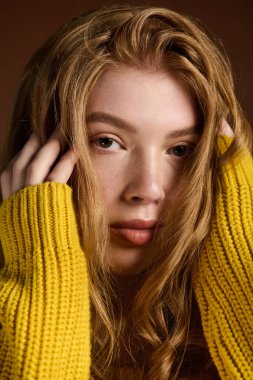 Genç, kızıl saçlı bir kadın, hoş bir kış kazağıyla, sıcak kahverengi bir arka fona karşı zarifçe poz veriyor..