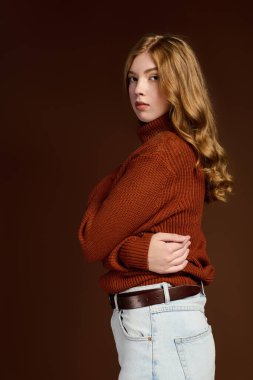 Genç bir kızıl, örgü örülmüş bir kazakla poz veriyor. Stüdyo ortamında gündelik kıyafetlerini sergiliyor..