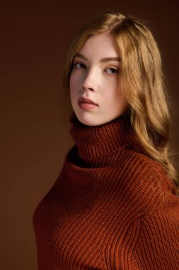 Kışlık süveter giyen güzel bir kızıl, stüdyo ortamında rahat poz veriyor..