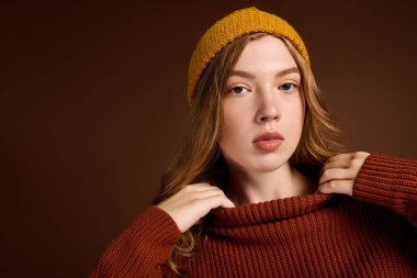 Genç bir kızıl, rahat bir kış kazağı ve parlak bir bereyle rahatça poz verir..