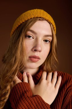 Genç bir kızıl saçlı, sıcak tonlarla dolu bir stüdyo ortamında şık bir kış modası sergiliyor..