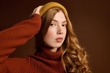 Şık bir kış kazağı giyen kızıl saçlı rahat bir stüdyo ortamında kendine güvenen pozlar veriyor..
