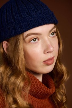 A redhead young woman poses with a charming expression in a winter sweater, looking stylish.