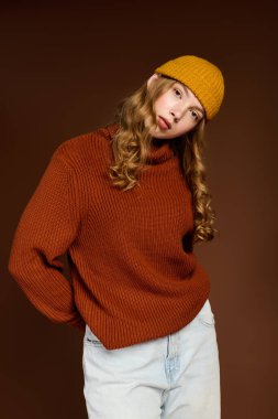 Sade süveter giyen genç bir kızıl, kahverengi bir fonda kış modasını sergiliyor..