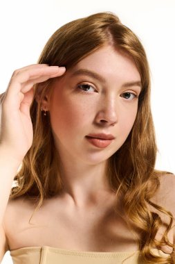 Güzel kızıl saçlı genç bir kadın parlak bir stüdyoda doğal makyajını ön plana çıkarıyor..