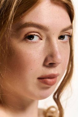 Kendine güvenen genç bir kızıl, parlak beyaz bir stüdyoda doğal makyajını sergiliyor..