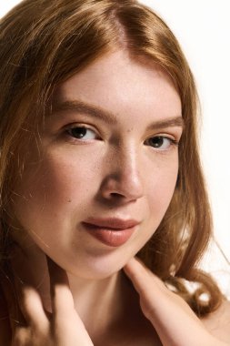 Doğal makyajlı genç bir kızıl parlak beyaz bir stüdyoda zarifçe poz veriyor..