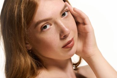 Genç bir kızıl, doğal makyajlı parlak beyaz bir stüdyoda zarifçe poz veriyor..