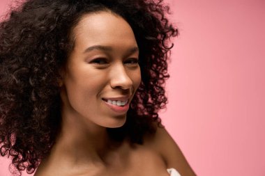 Kıvırcık saçlı güzel genç bir kadın canlı pembe bir fon karşısında bir anlık sevinçten zevk alıyor..